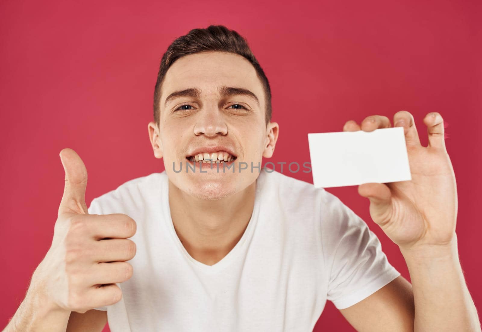 A guy with a business card in his hand gestures and emotions red background. High quality photo