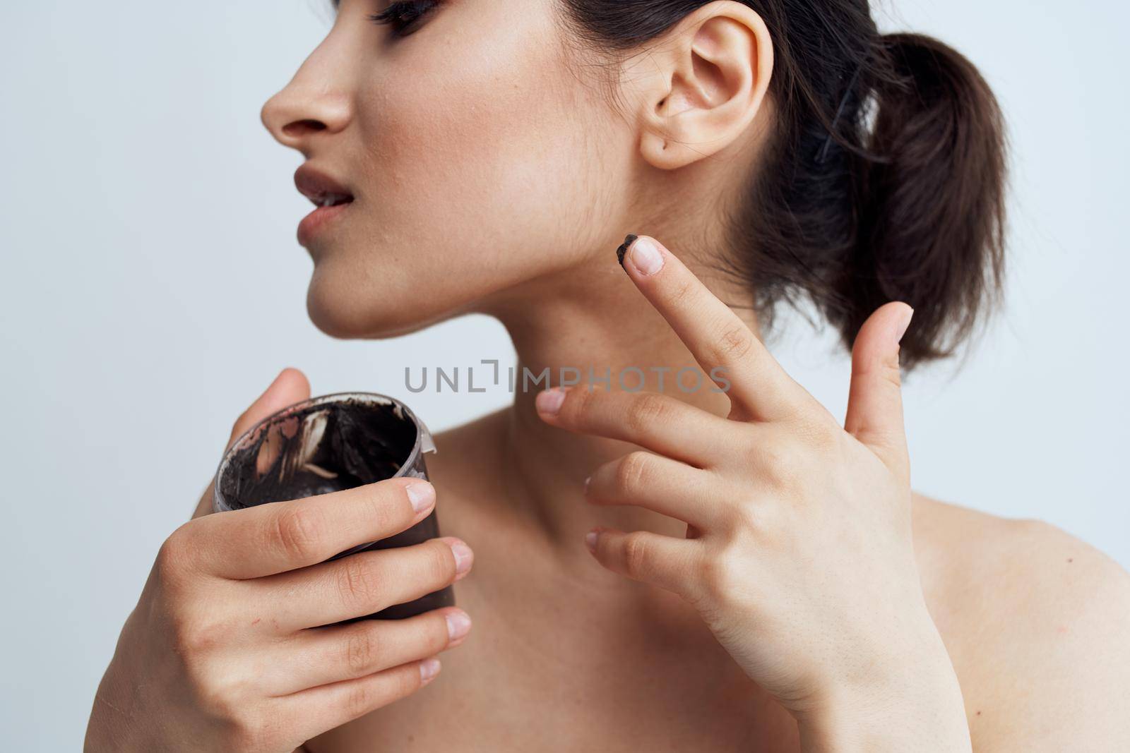 Pretty brunette naked shoulders black cream skin care close-up. High quality photo