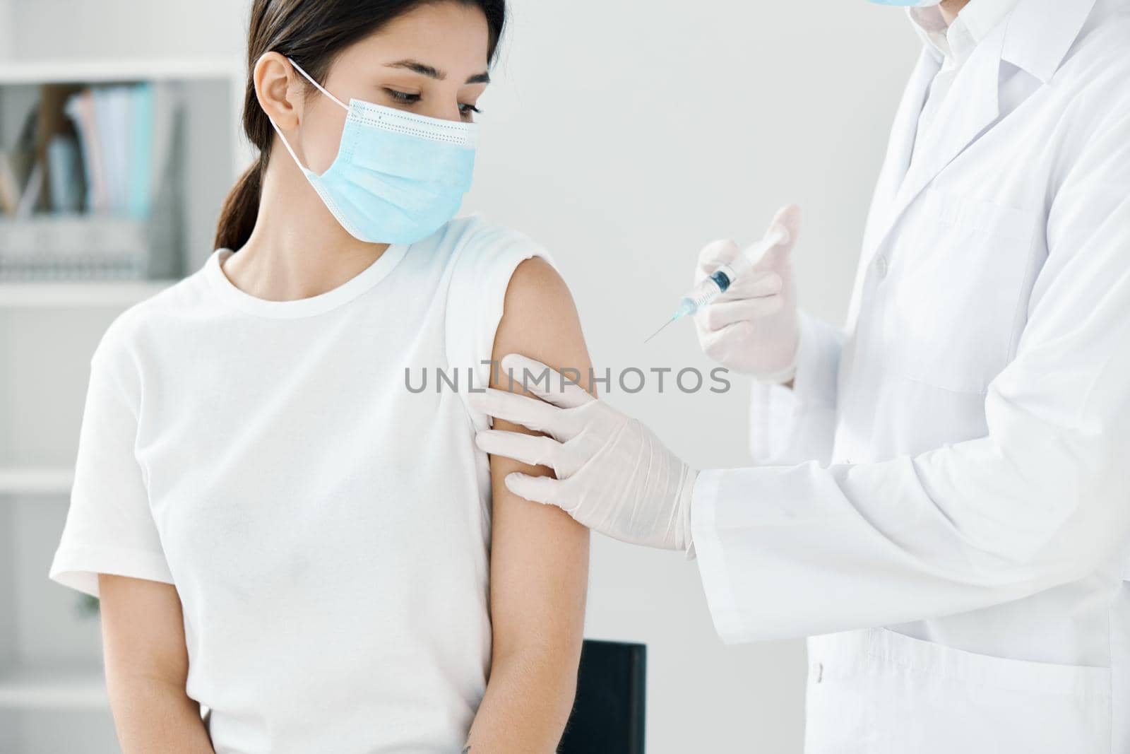 doctor in a medical gown and a mask injecting a woman in the shoulder. High quality photo