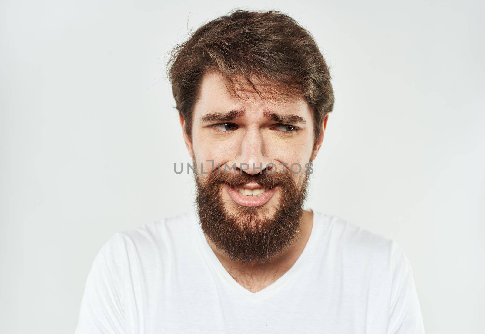 Bearded man in a white T-shirt on a light background sad face emotions beard. High quality photo