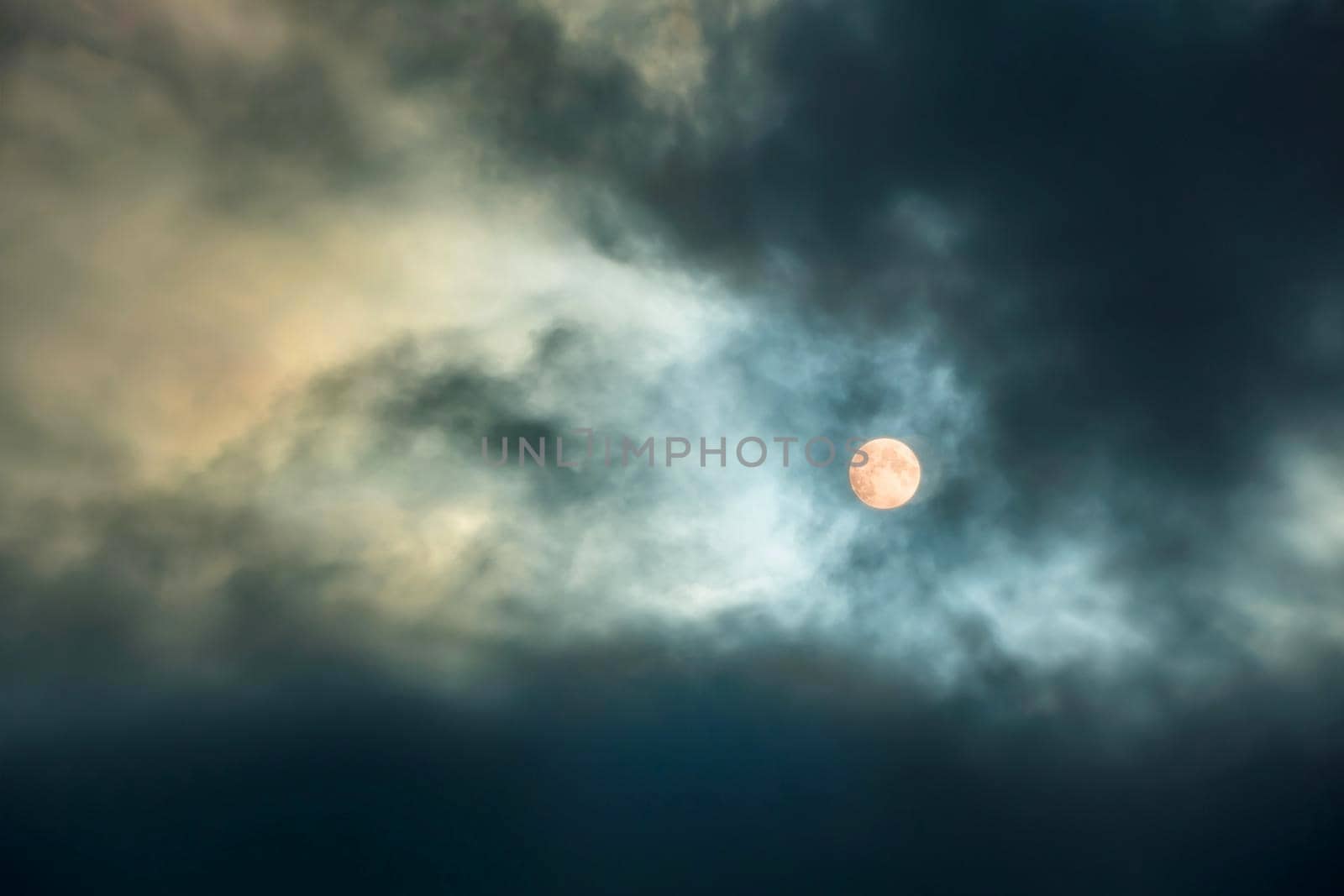 A large moon in a cloudy sky with thick clouds. Full moon. The night sky with the bright light of the full moon.Clouds at night time by YevgeniySam