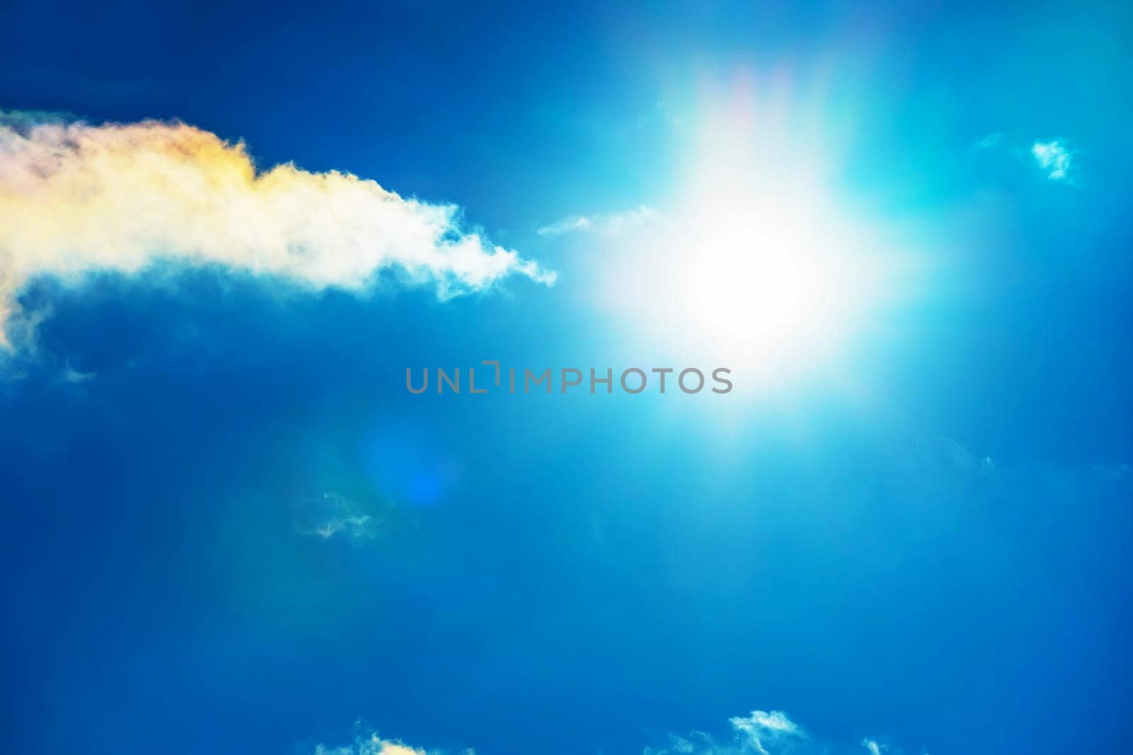 The sun in the blue sky under the clouds. Sunny day. Blue sky. Bright midday sun illuminates the space. Blue sky with clouds and sun reflection. The sun shines bright in the daytime in summer. by YevgeniySam