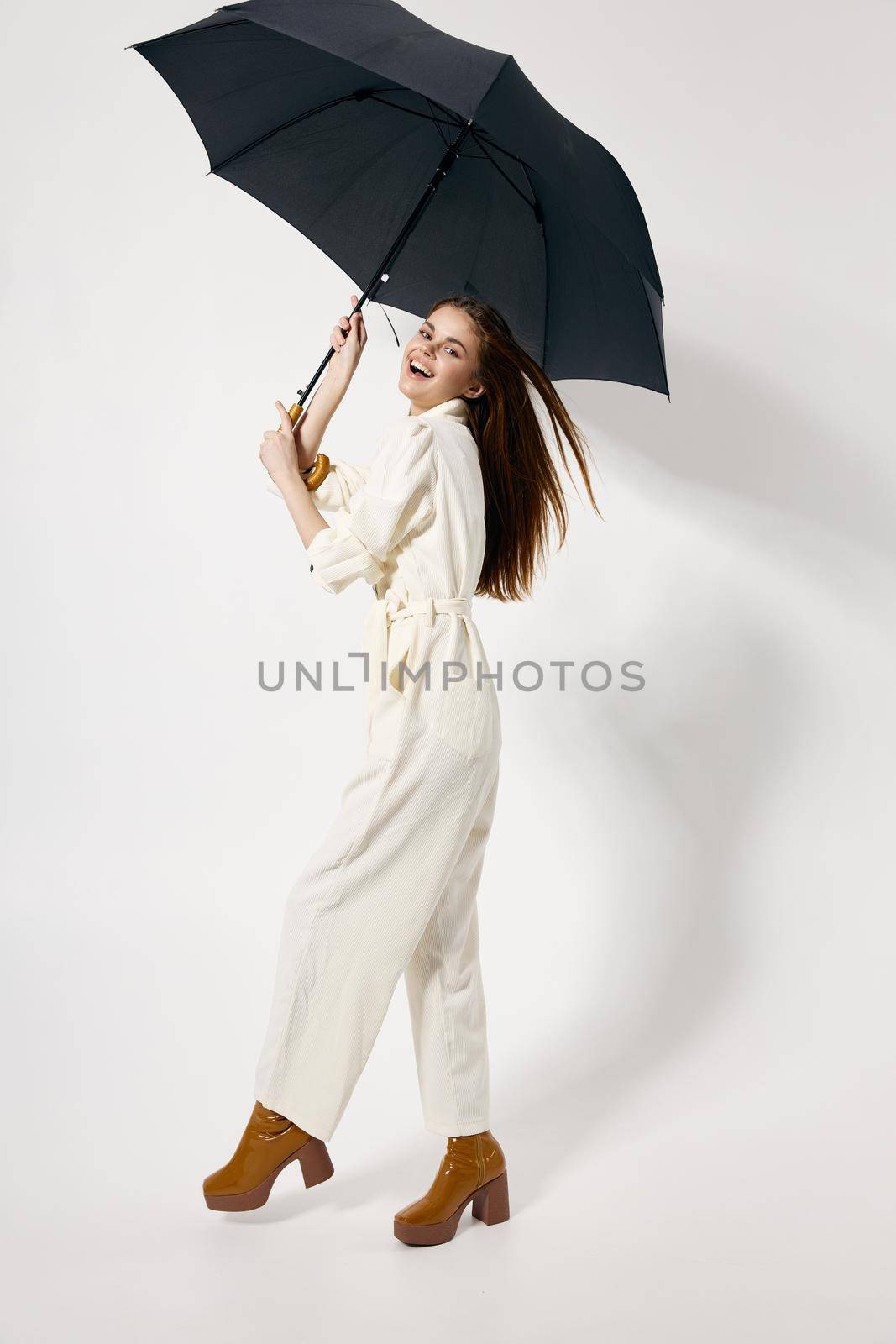 cheerful woman holding an umbrella in her hands white jumpsuit fashion studio boots. High quality photo