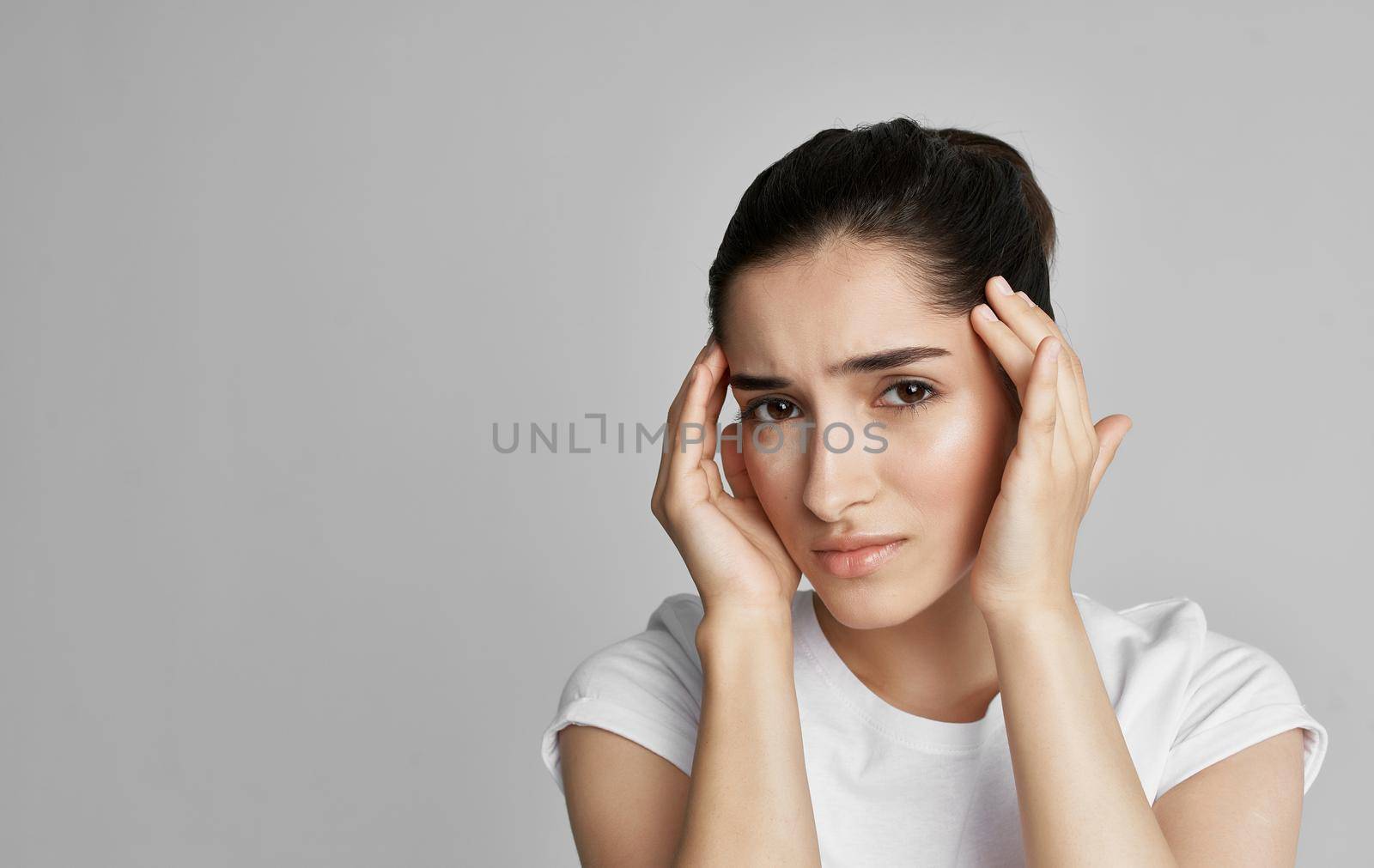 A woman in a white t-shirt holds her face with a headache and nigative health. High quality photo