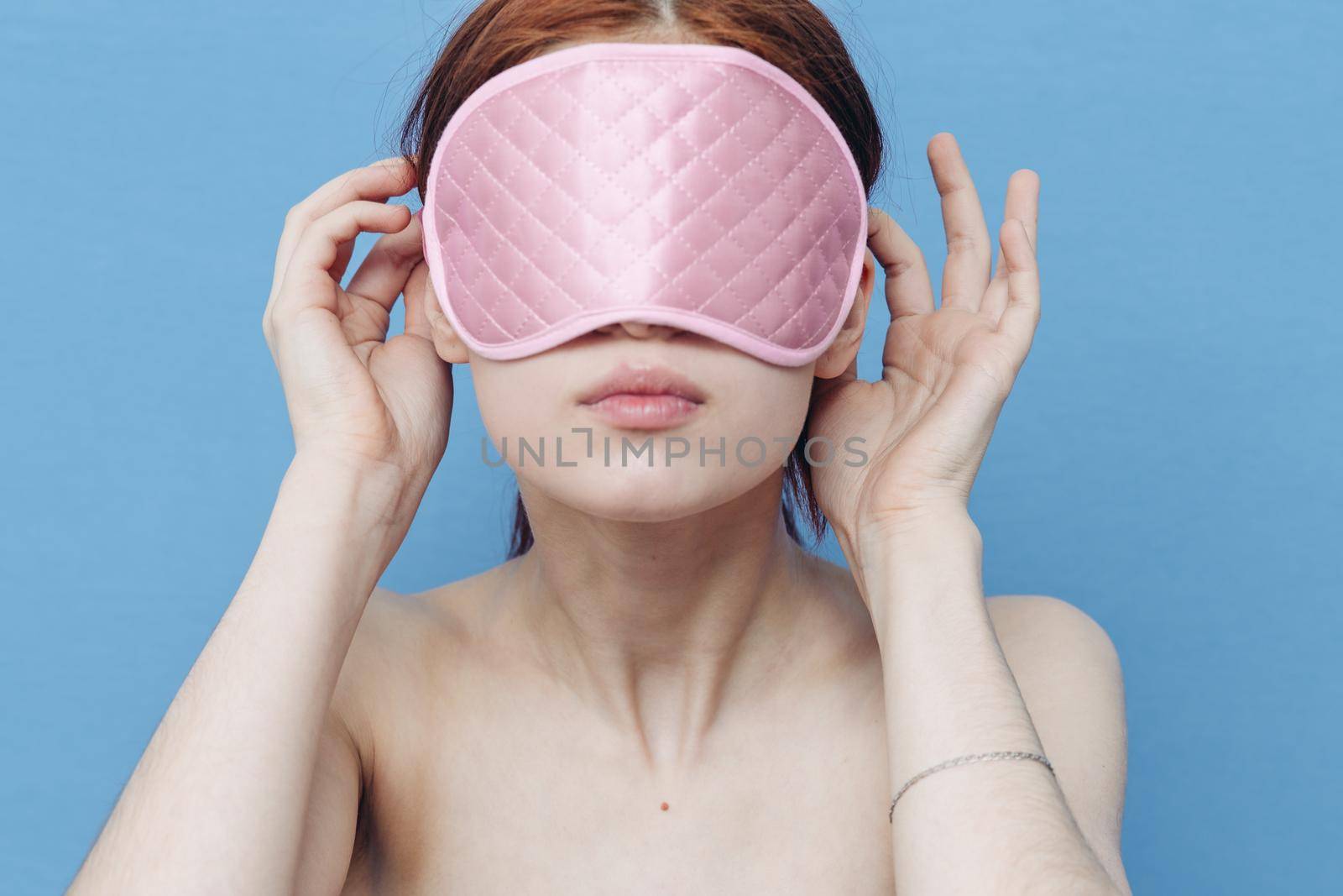 emotional woman with pink sleep mask on her face and blue background model. High quality photo