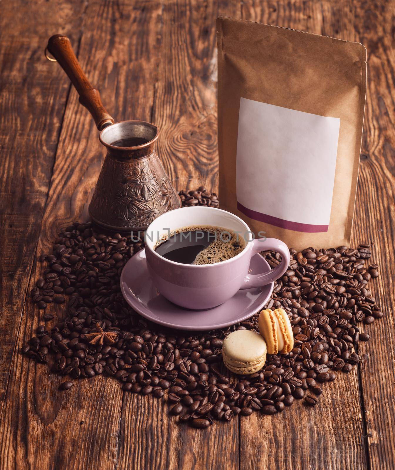 purple cup of coffee, macaroons, beans, turkish coffee pot, and craft paper pouch bag on wooden backgroun