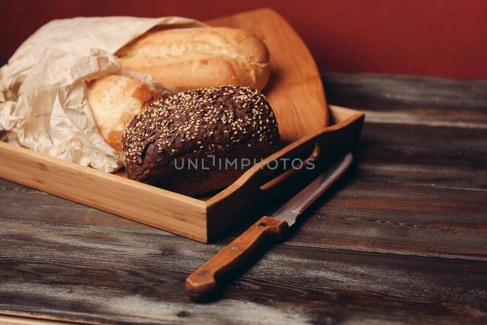 flour products rye bread on a tray and a sharp knife on a table on a red background. High quality photo