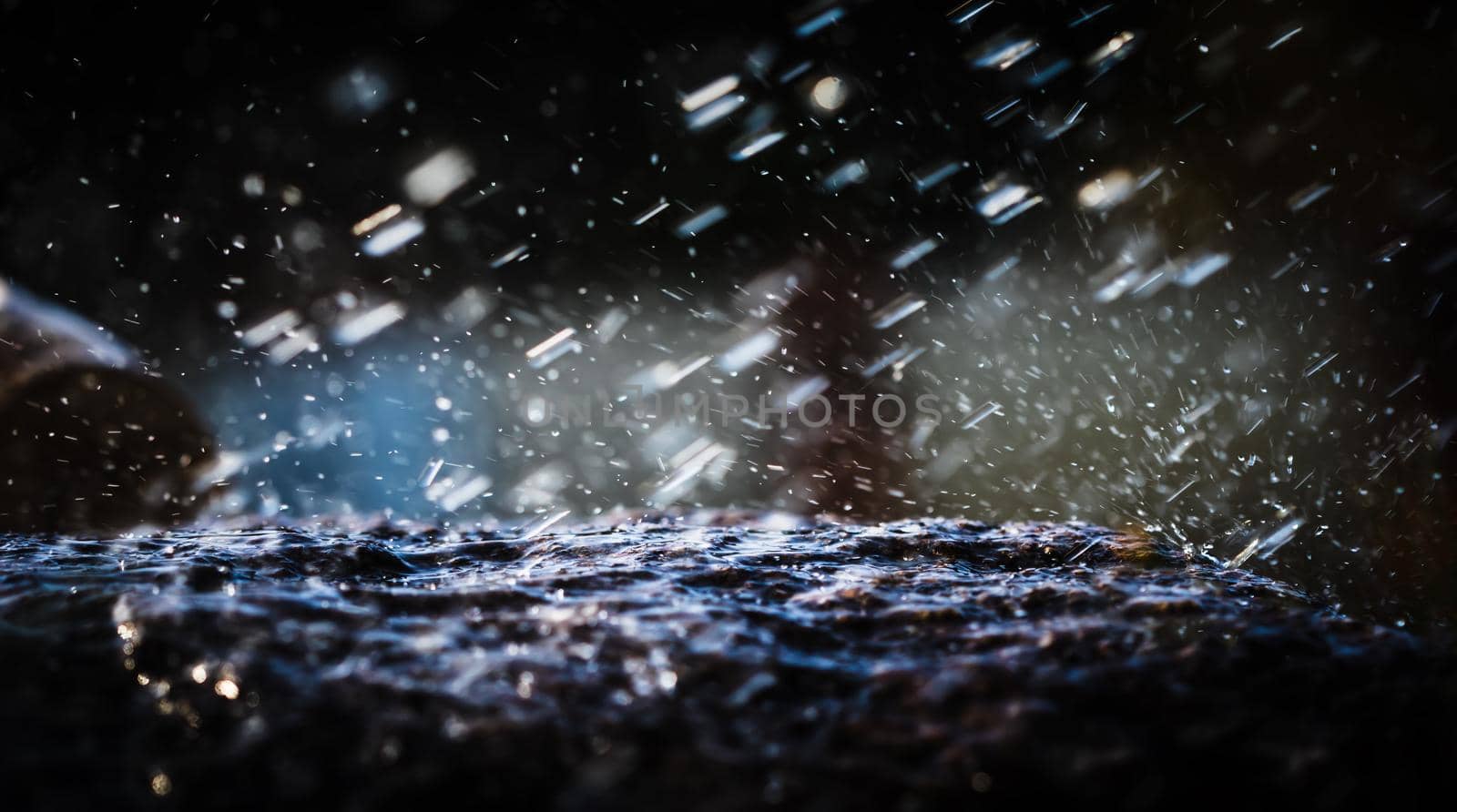 Wet stone in the rain. Rain water drop falling to the stone. Water is flowing and splashing around them.