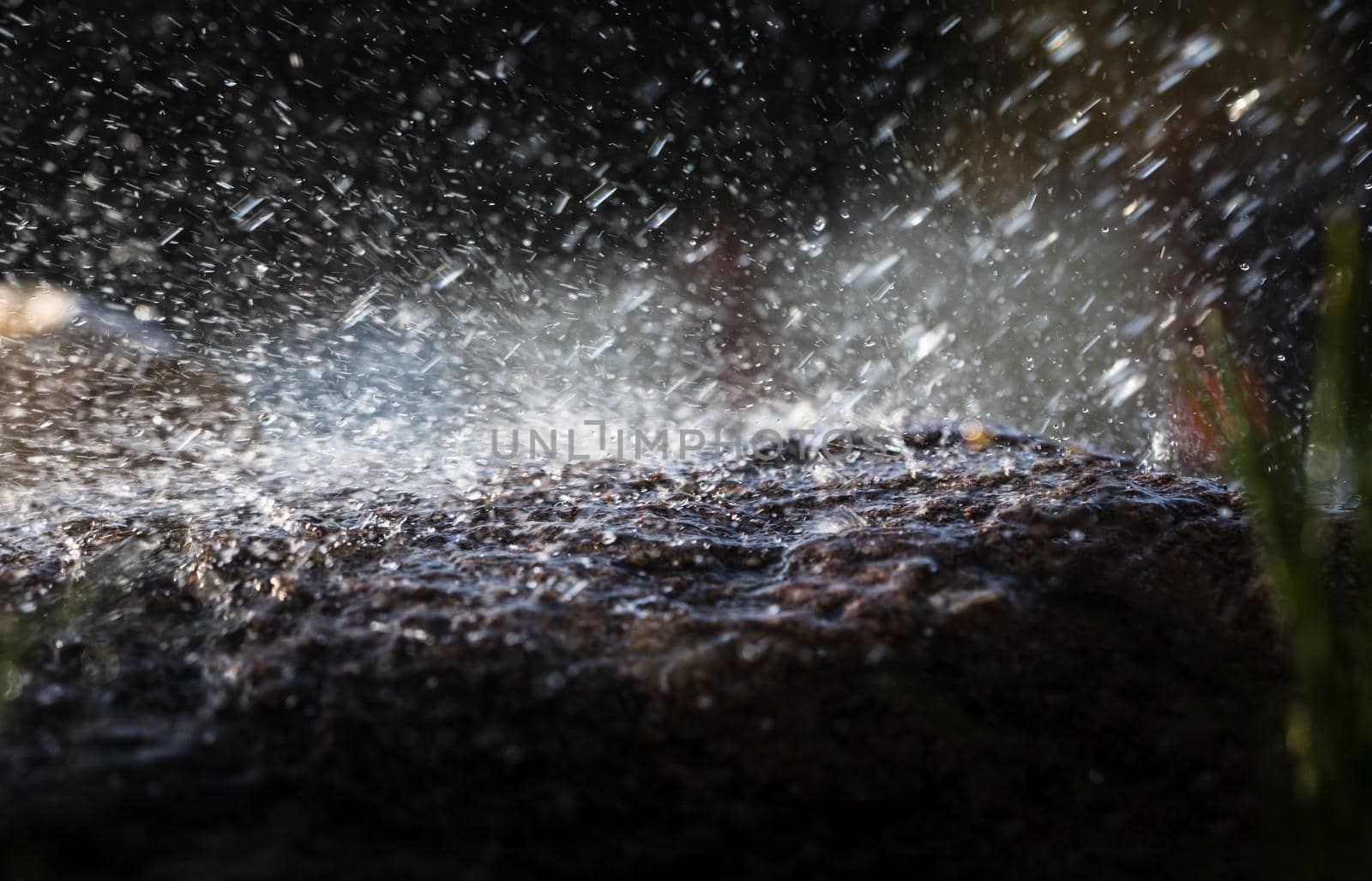 Wet stone in the rain. Rain water drop falling to the stone. Water is flowing and splashing around them.