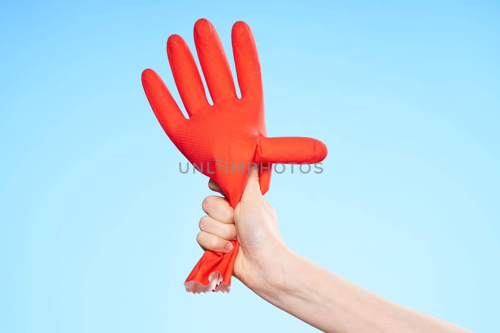 inflated rubber red glove in hand blue background and house cleaning by SHOTPRIME