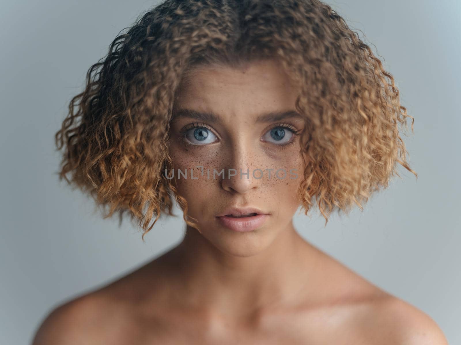 Beautiful woman portrait light background bared shoulders curly hair. High quality photo