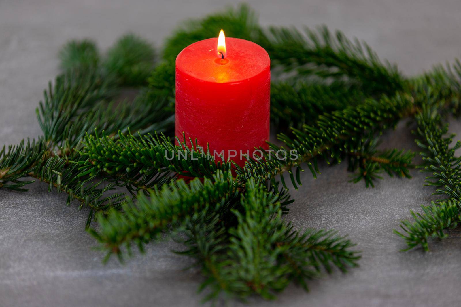 Christmas motif, texture, background with branches of a Nordmann fir and burning red candle on a dark grey marbled  background. by reinerc