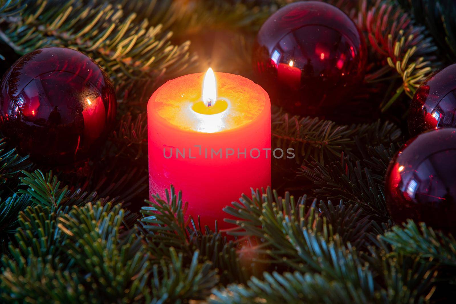 Atmospheric christmas motif with red burning candle surrounded by Nordmann fir branches, red christmas tree balls and gift parcel