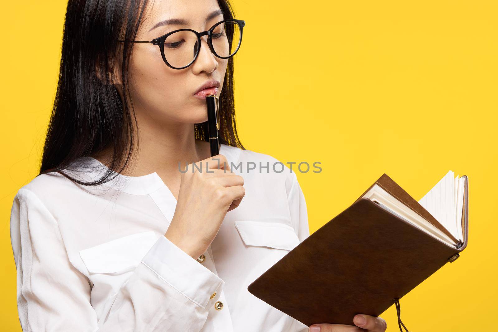 pretty brunette with glasses holding a notebook in the hands of students learning yellow background. High quality photo