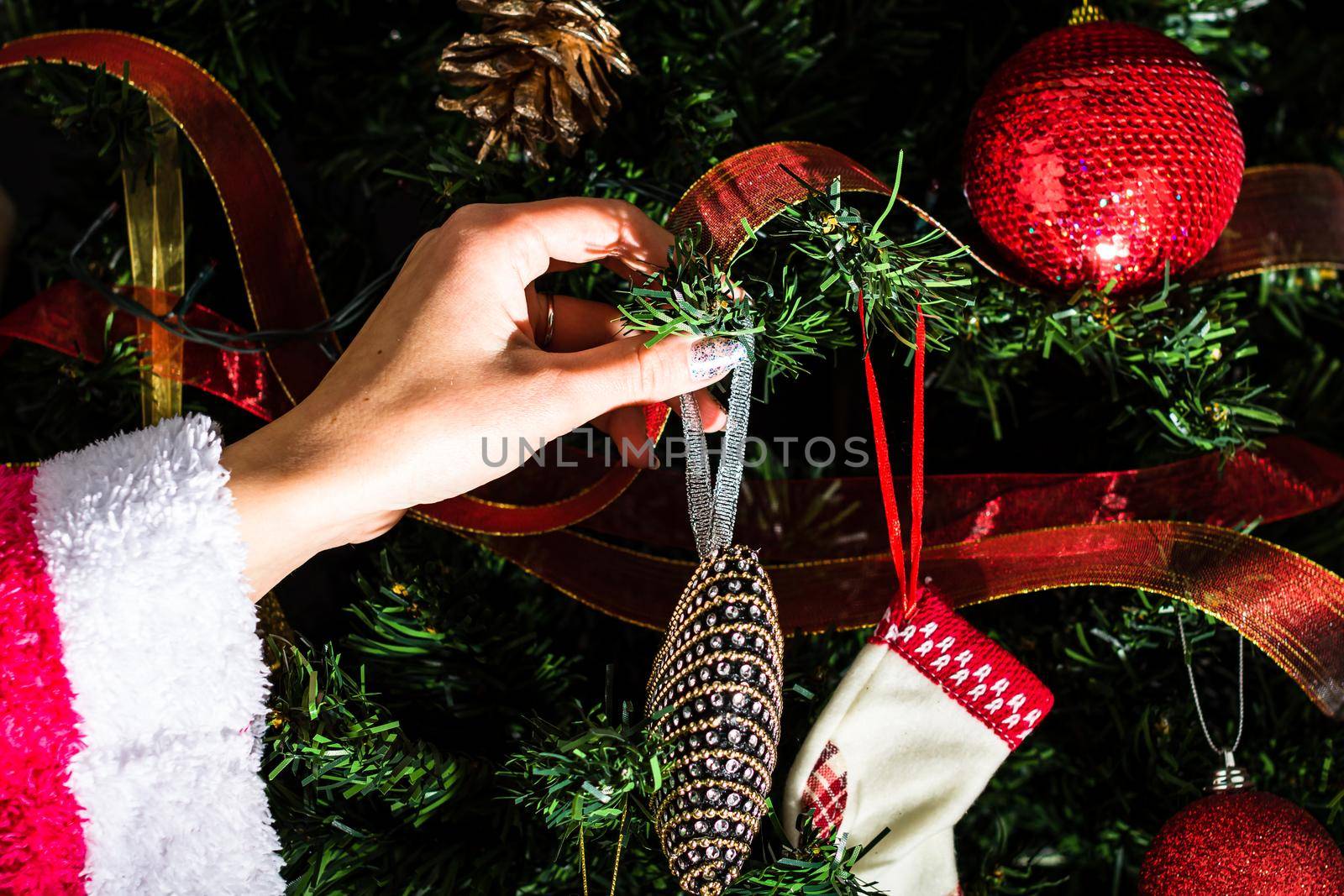 Decorating Christmas tree, hand putting Christmas decorations on fir branches. Christmas hanging decorations.