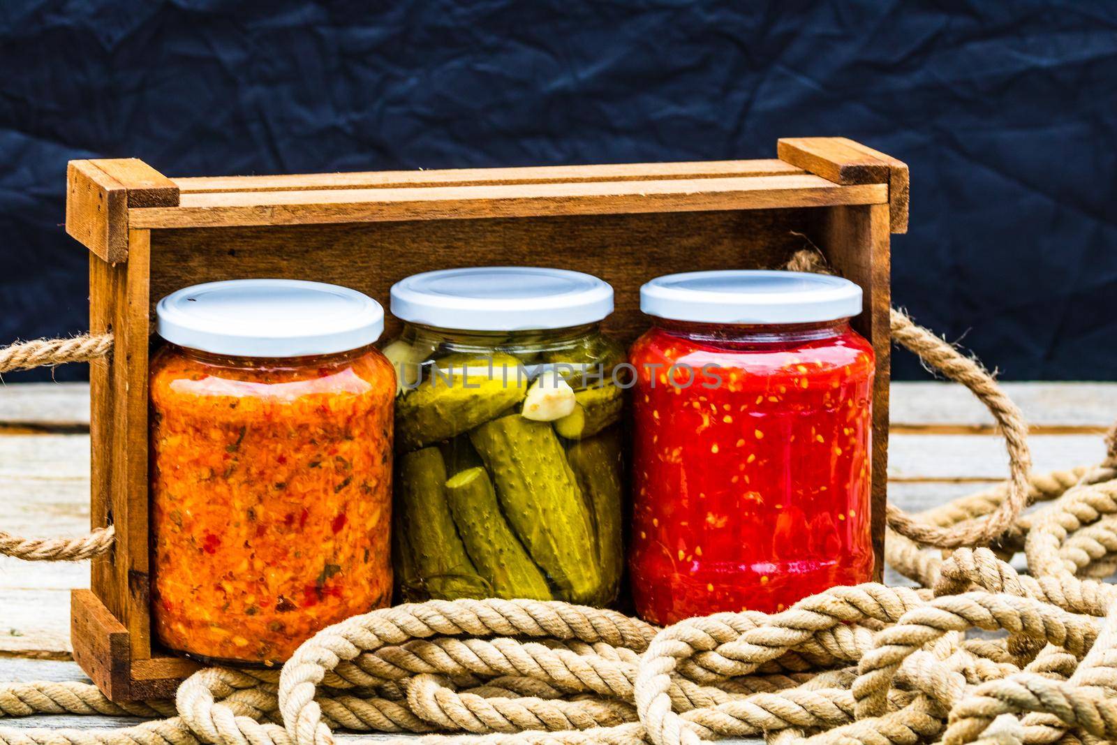 Wooden crate with glass jars with variety of canned vegetables isolated.