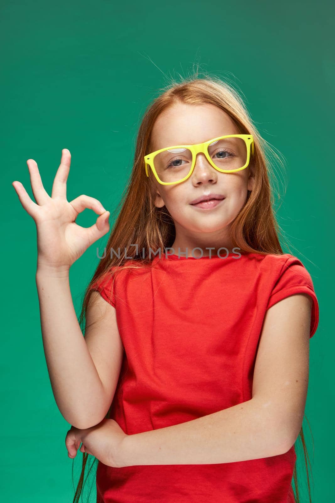 redhead girl with yellow glasses gesturing with her hands childhood learning Green background. High quality photo