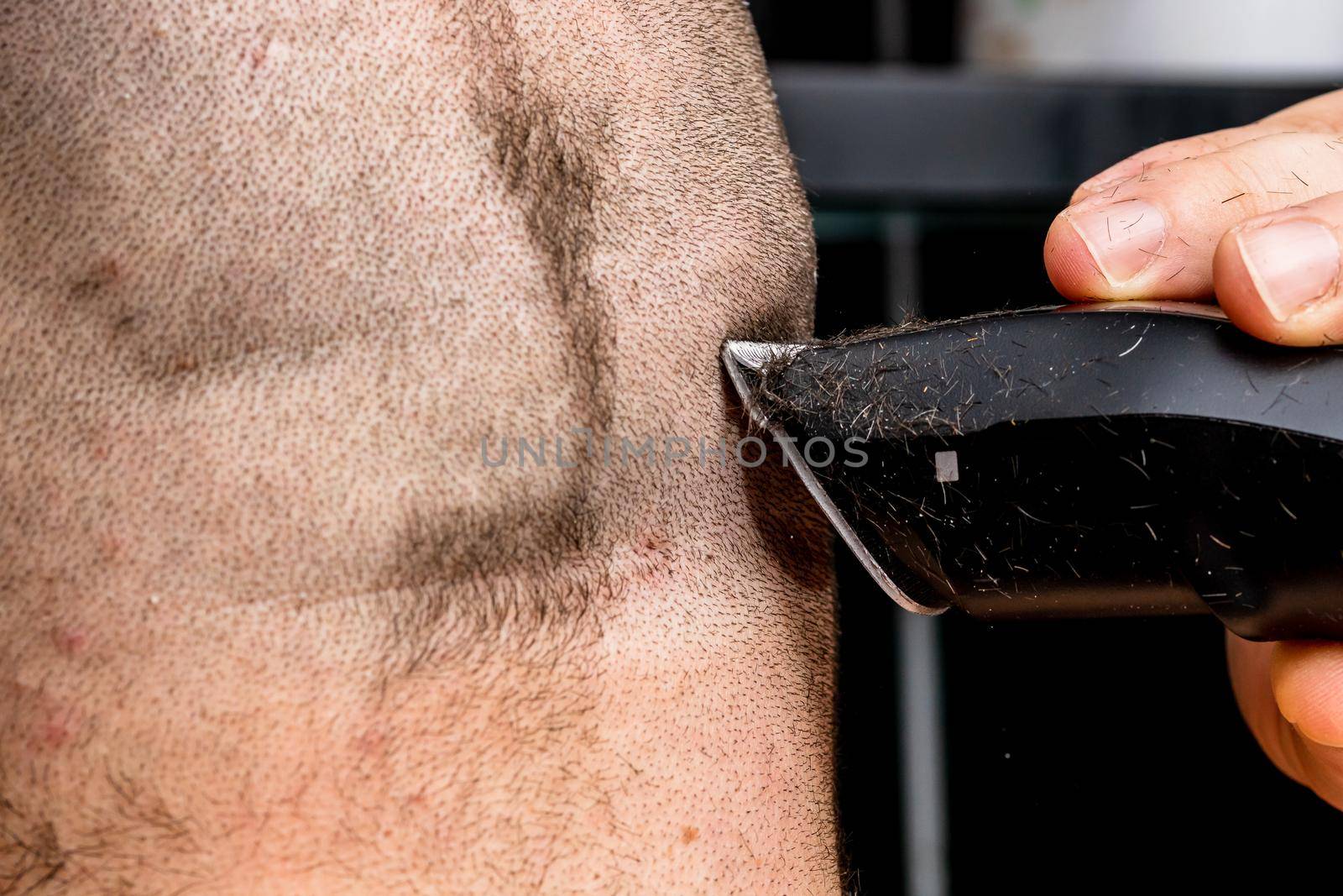 Man shaving or trimming his hair using a hair clipper by vladispas