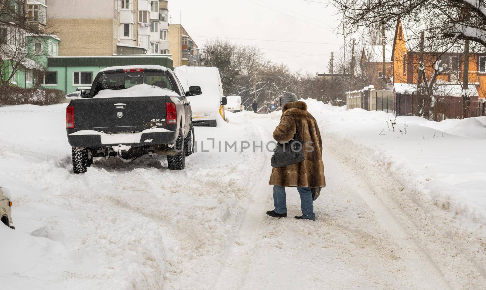 Lutsk, Ukraine - February 12,2020: Uncleaned slippery roads and sidewalk in winter. Cars in snowdrift. People on street after snow storm. City street after blizzard. Record-breaking amounts of snow