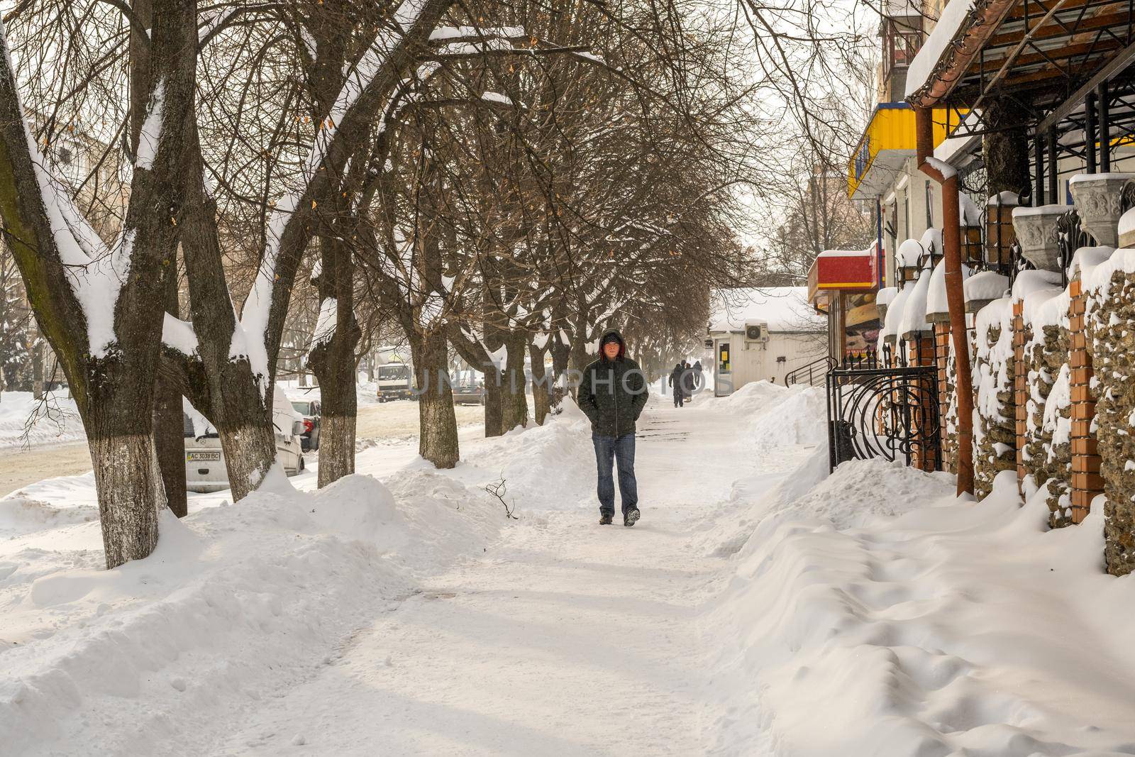 Lutsk, Ukraine - February 12,2020: People on street after snow storm. City street after blizzard. Record-breaking amounts of snow. Uncleaned slippery roads and sidewalk in winter. Cars in snowdrift