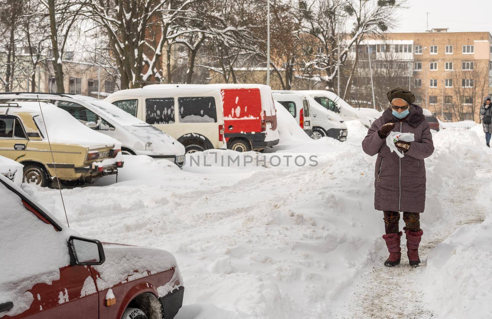 Lutsk, Ukraine - February 12,2020: City street after blizzard. Record-breaking amounts of snow. Health protection. Woman wearing face mask on public street in middle of coronavirus epidemic in winter
