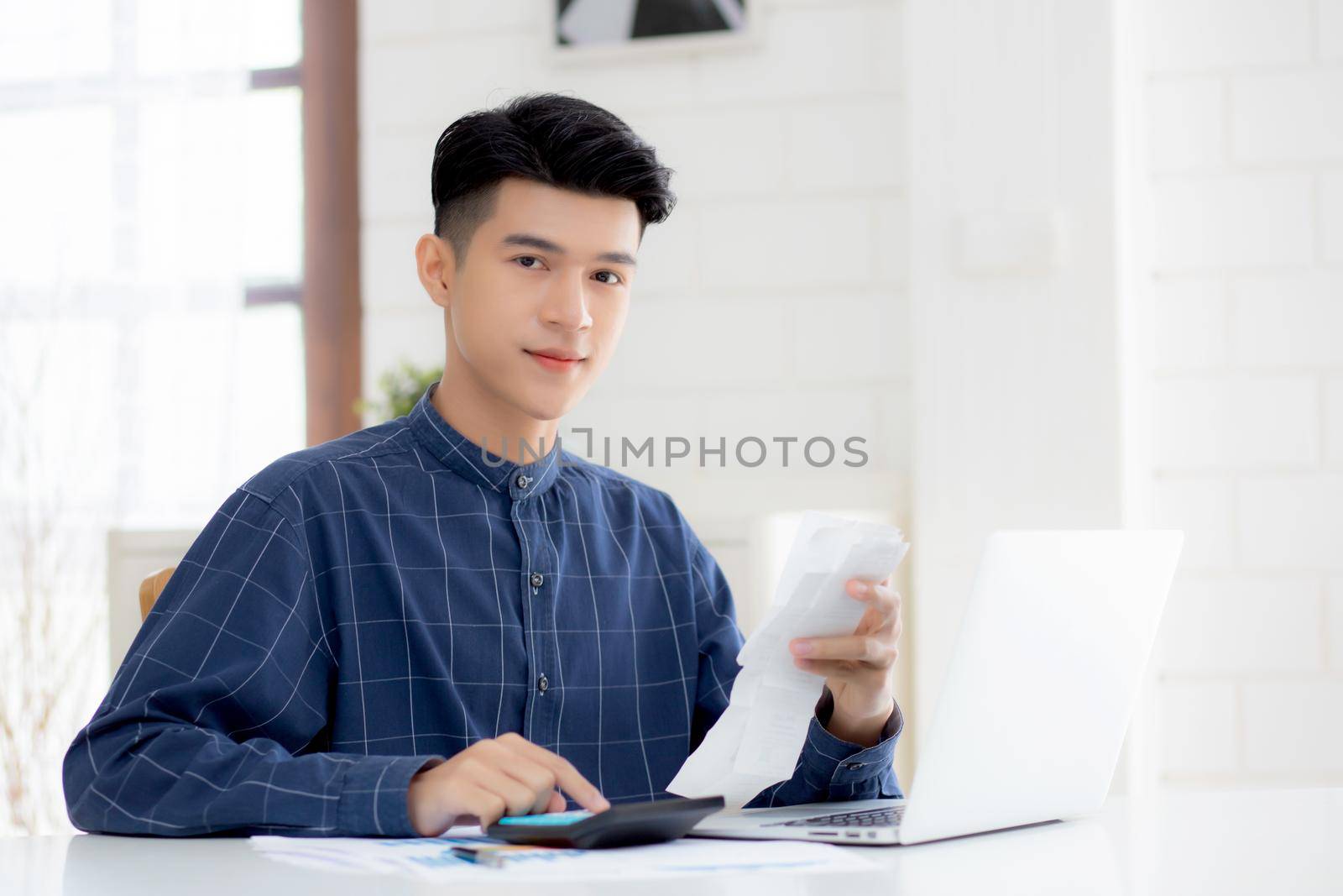 Young asian man calculating finance household with calculator on desk at home, male checking bill and success for saving expenses household, debt closure, tax and accounting, business concept.