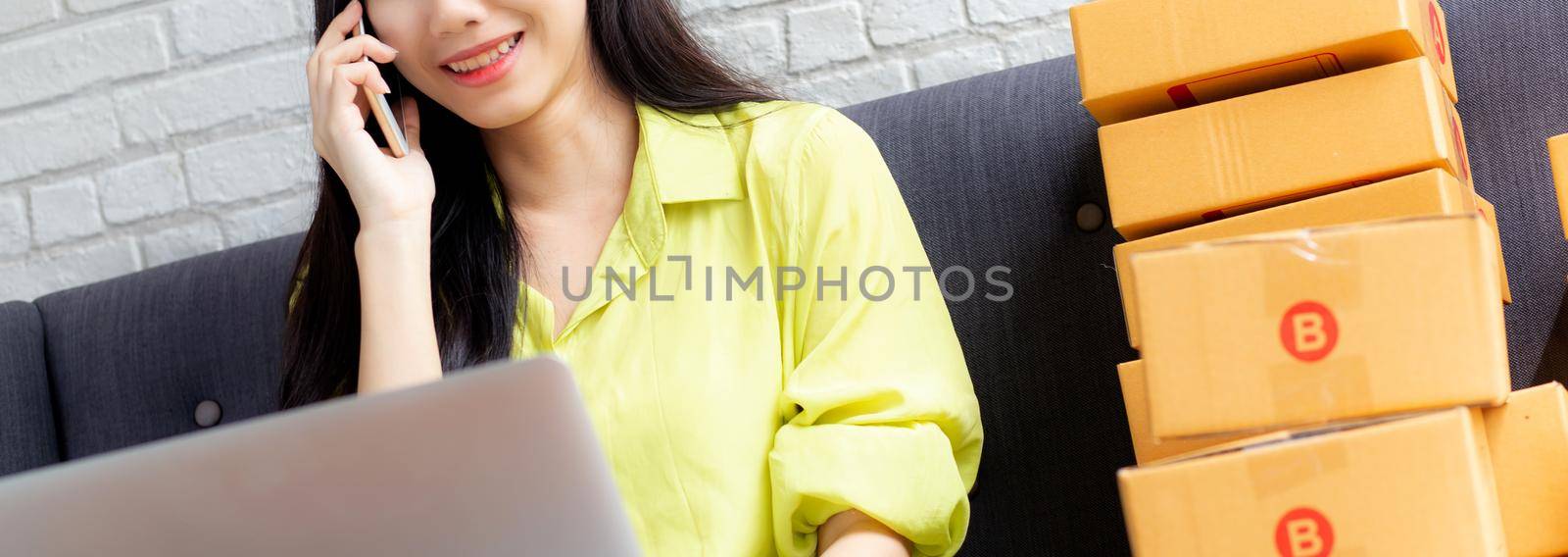 Young asian woman is entrepreneur talking with customer and using laptop computer while order purchase online at home, logistic and delivery, online shopping, female is seller of business SME.