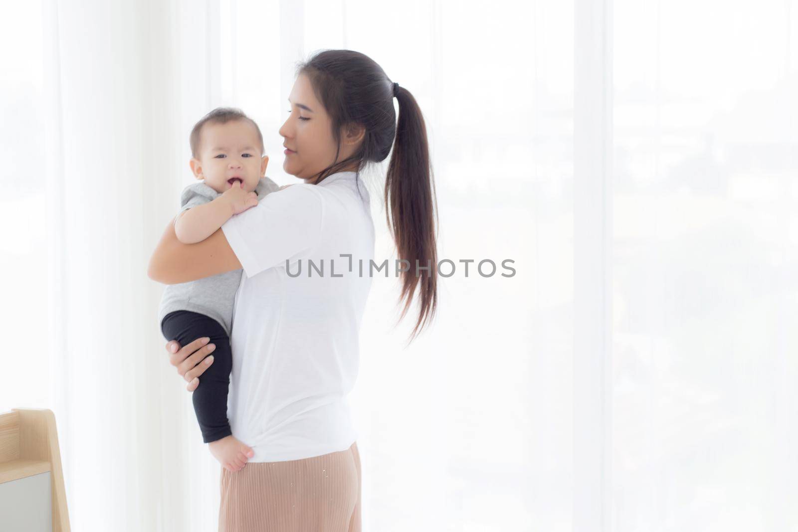 Young asian mother holding little baby girl and walking together in the bedroom at home, mom carry daughter and care, relationship of parent and child, toddler and parent, indoor, family concept.