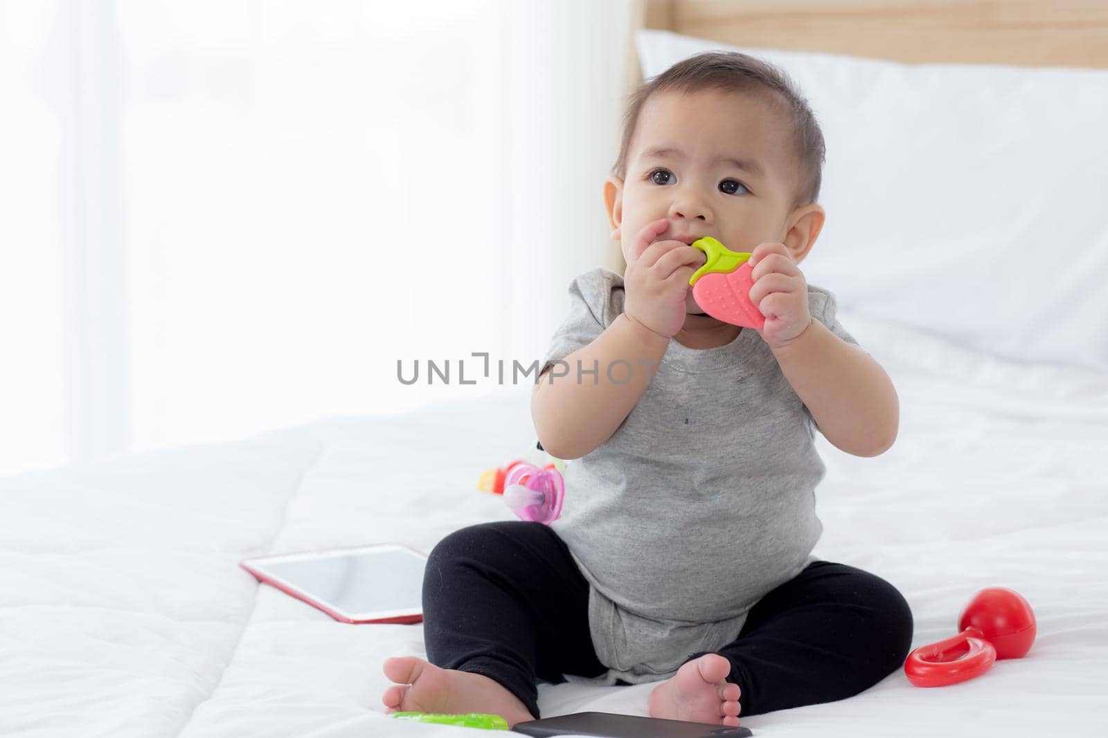 Portrait of cute little baby girl sitting with cozy on bed at bedroom, happiness of toddler, newborn 6-11 months with innocence and expression with cheerful, child charm, indoors, one person.