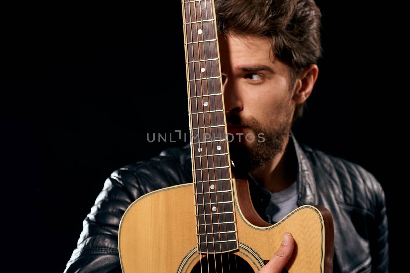 A man with a guitar in his hands leather jacket music performance rock star modern style dark background. High quality photo