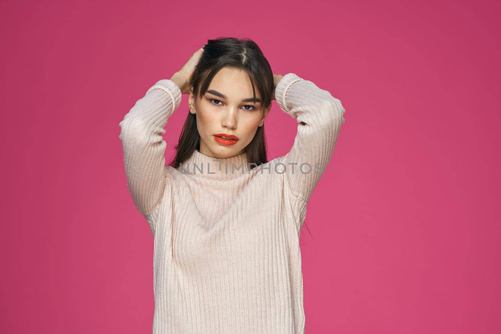 Brunette with long hair red lips cosmetics white sweater pink background cropped view. High quality photo