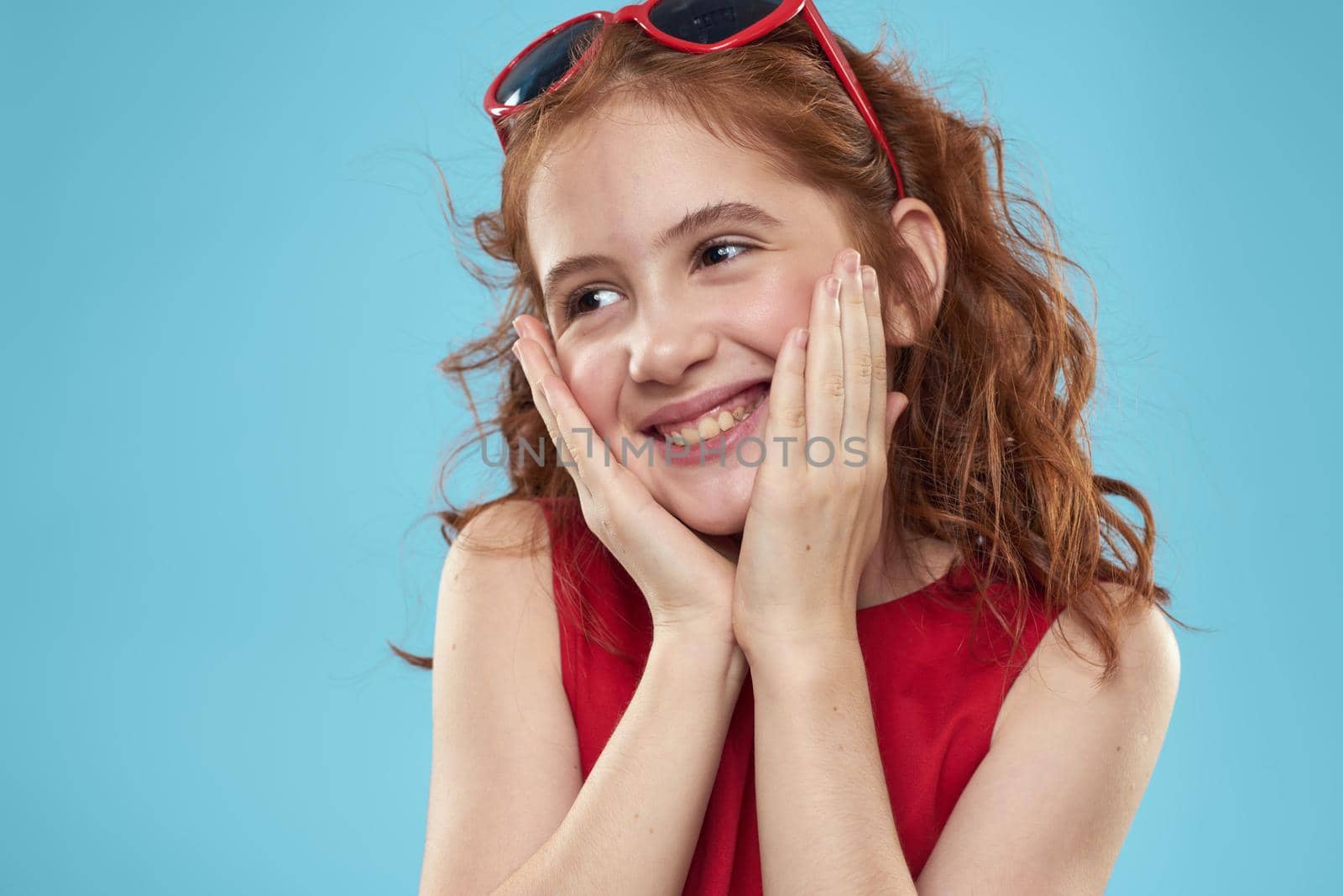 girl with curly hair sunglasses red dress and childhood fun blue background. High quality photo