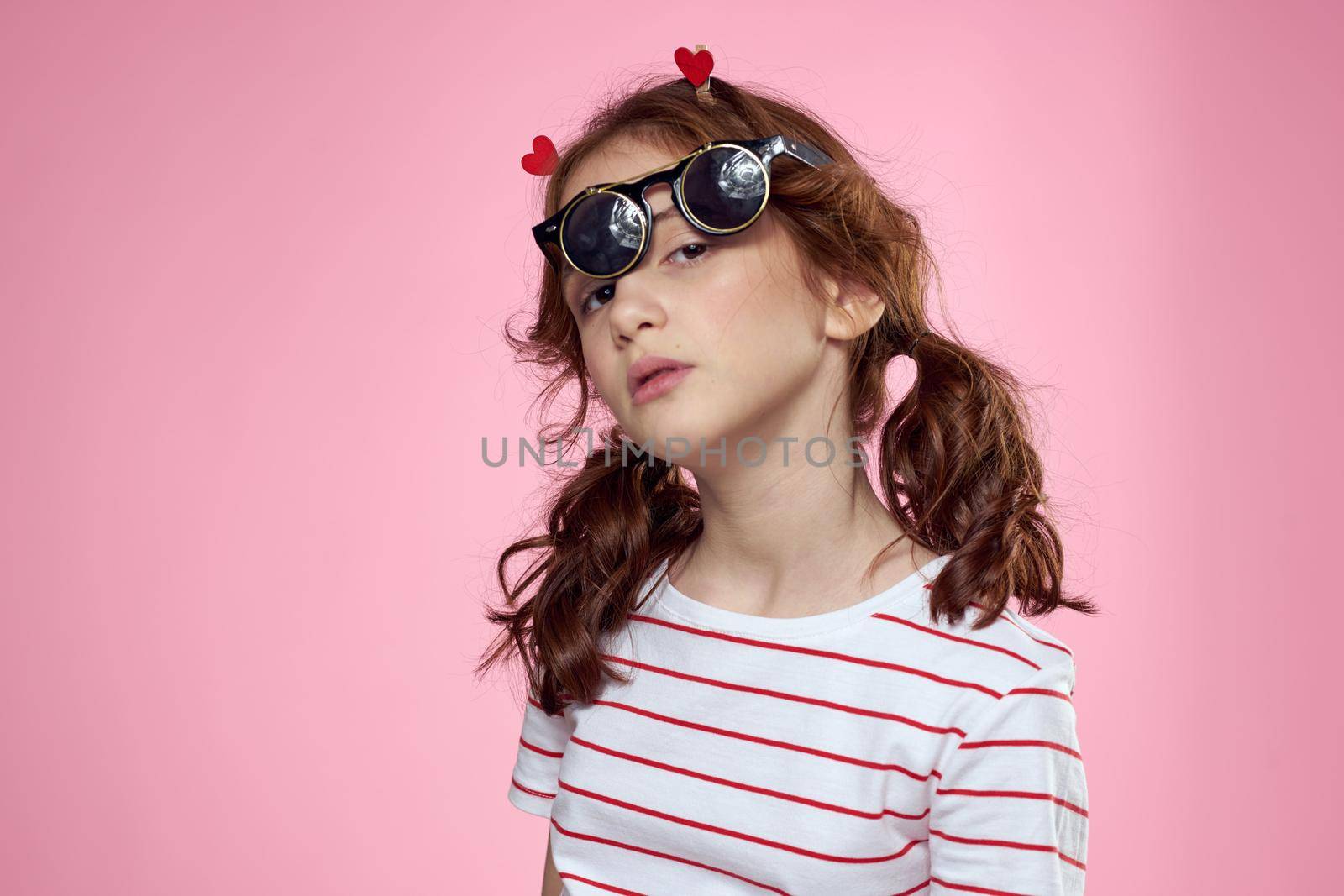 little girl in fashionable glasses and clothespins on her hair emotions pink background hearts. High quality photo