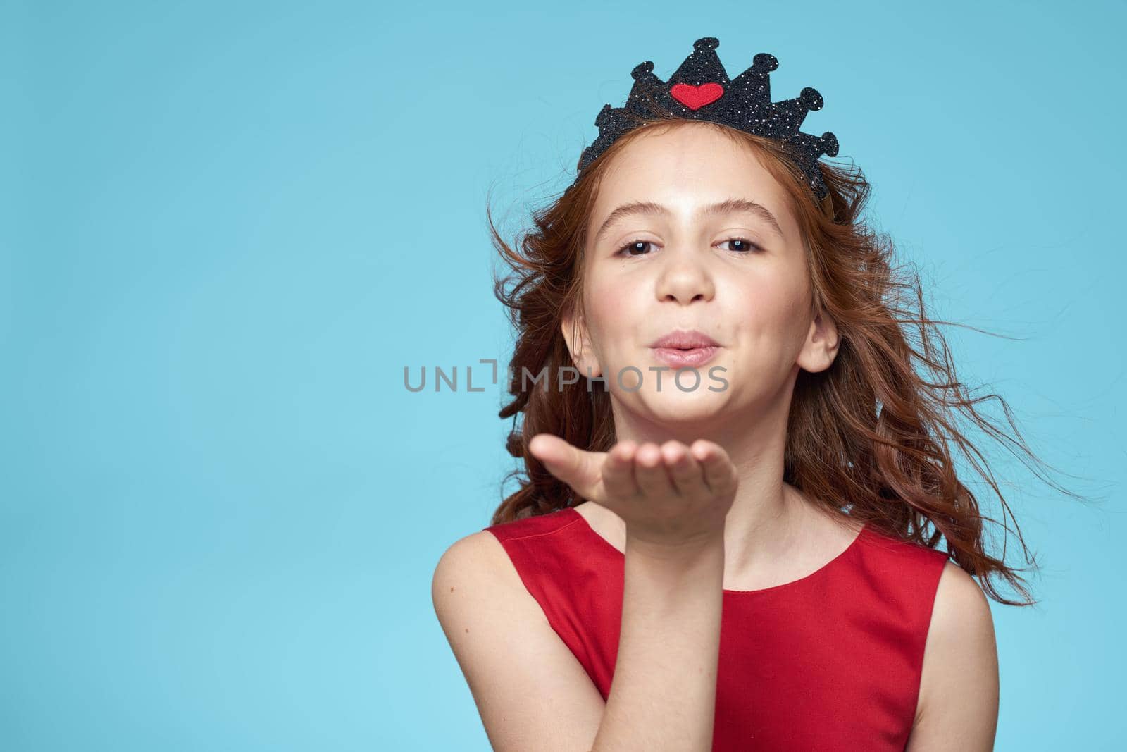 little girl with curly hair with a crown on her head red dress Smile blue background. High quality photo