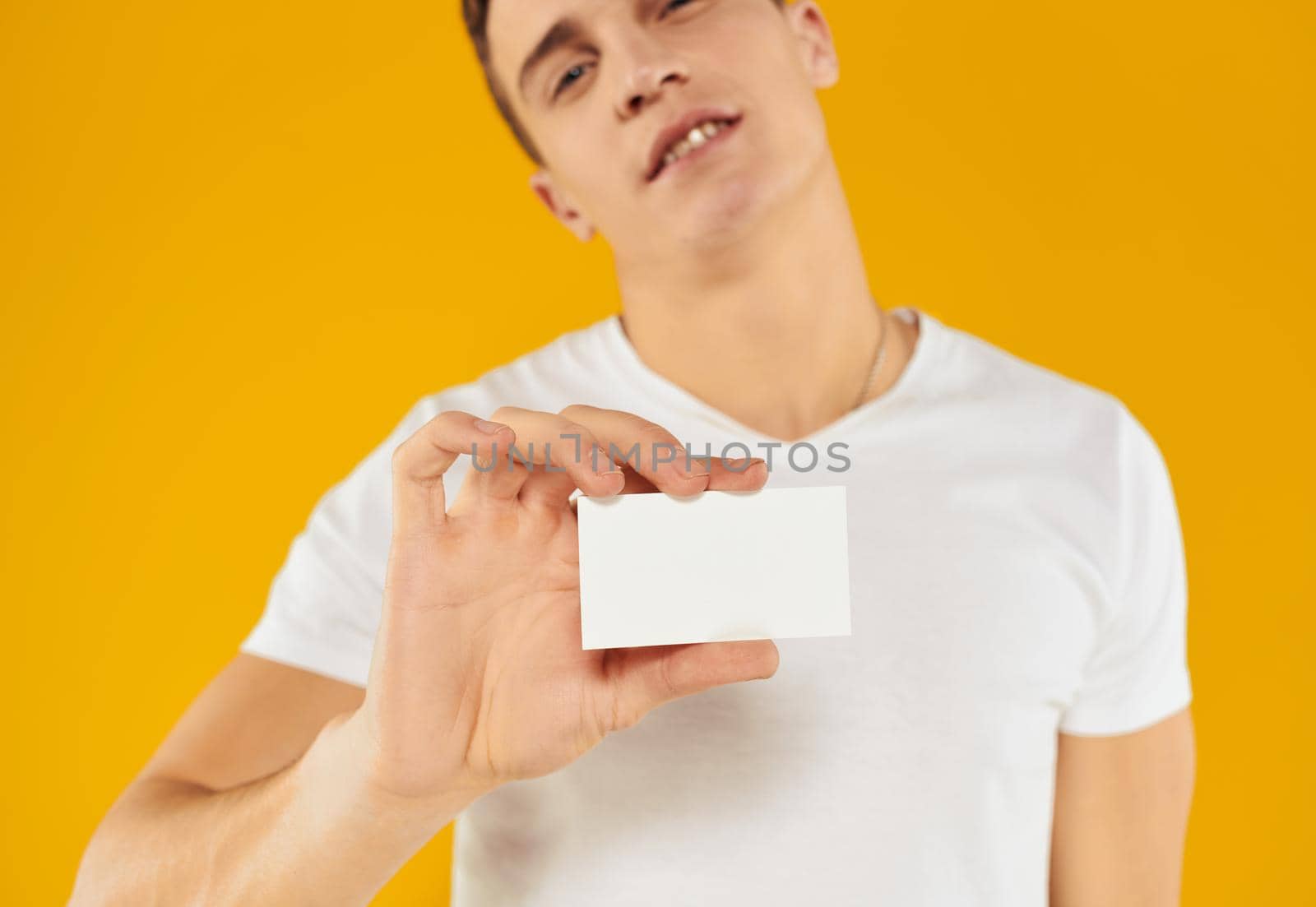 man in white t-shirt showing business card on yellow background cropped view. High quality photo