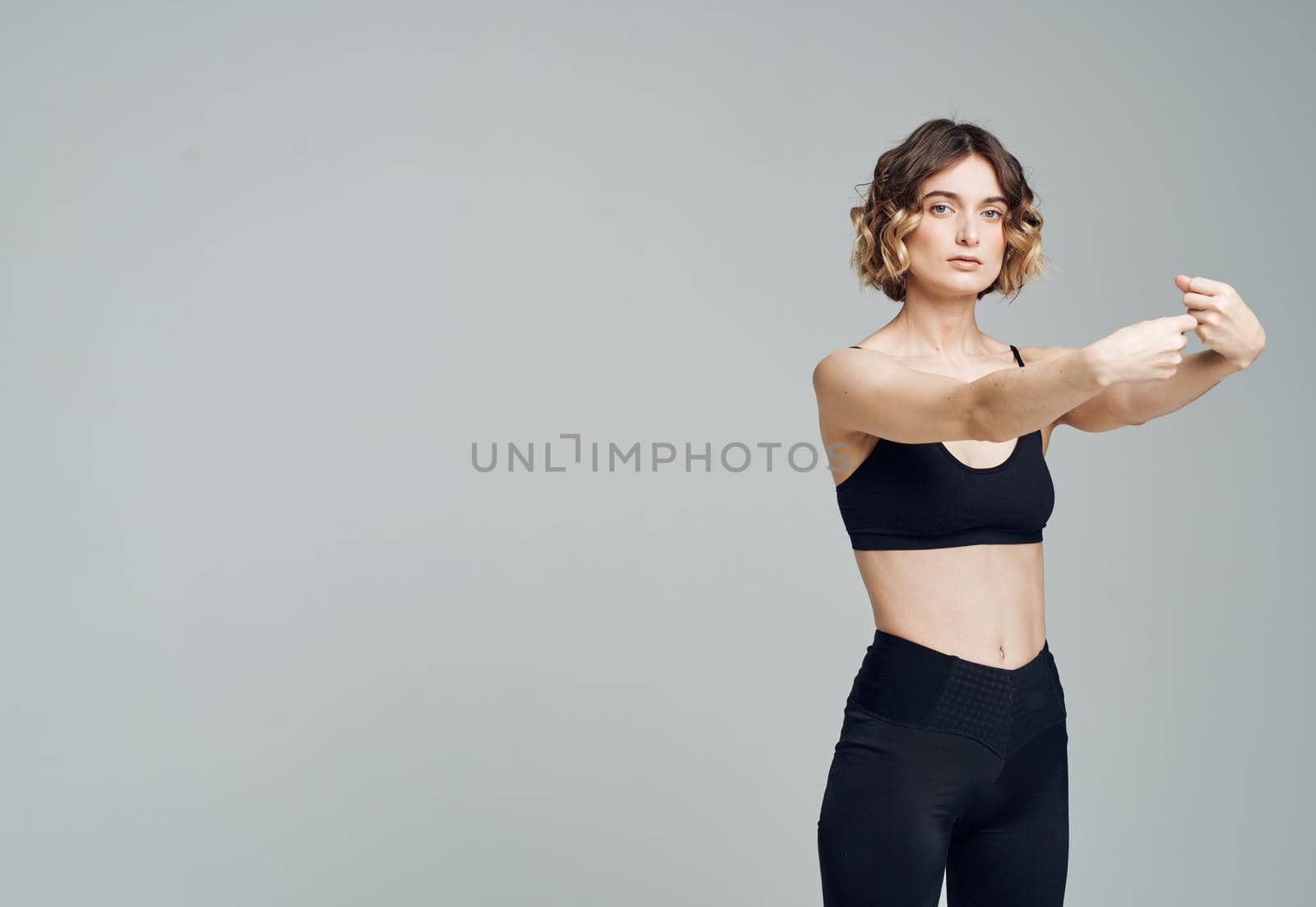 A woman in dark sportswear on a gray background gestures with her hands. High quality photo