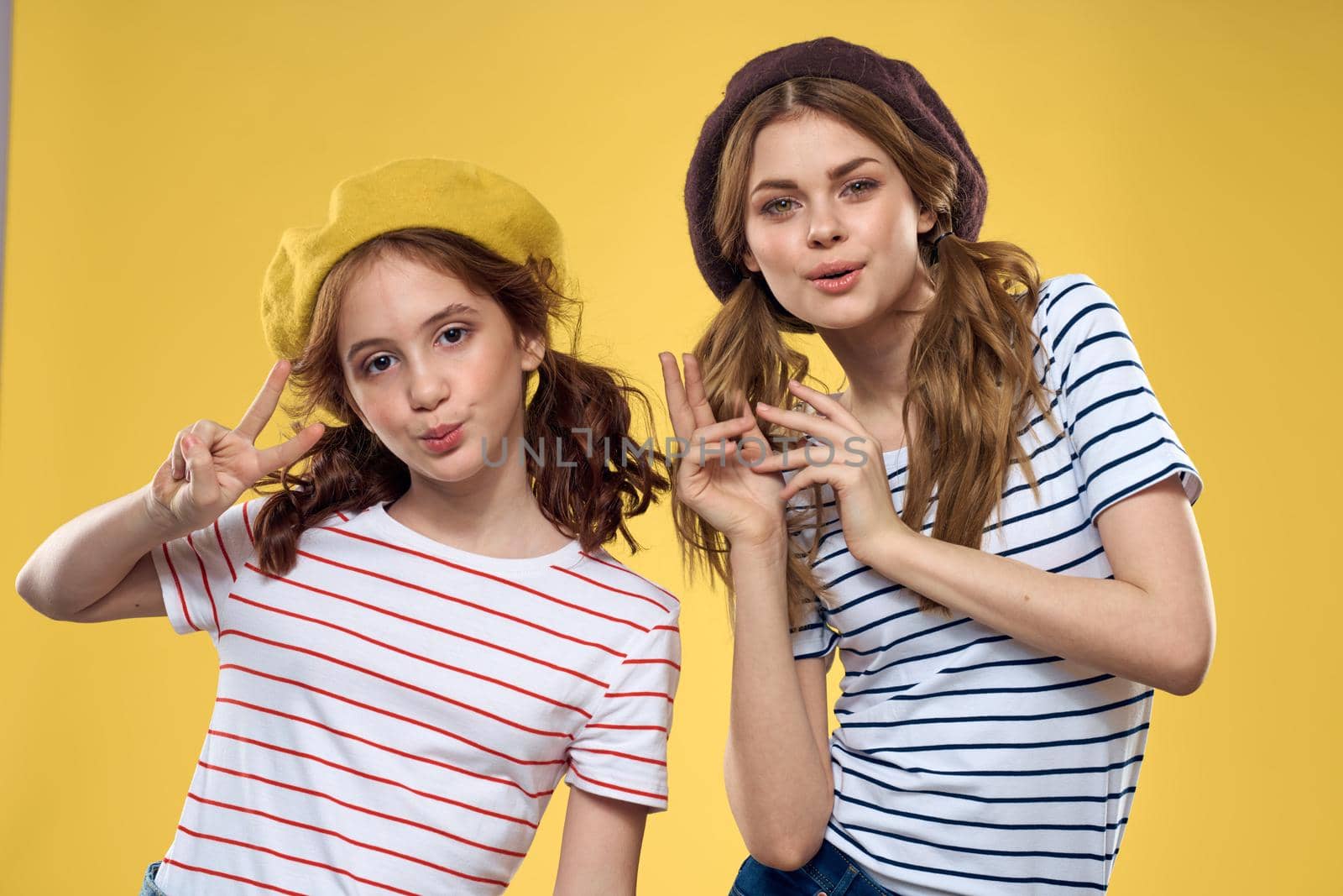 funny mom and daughter wearing hats fashion fun joy family yellow background. High quality photo