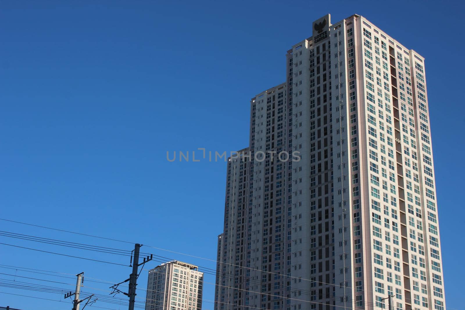 The wide-angle view of a skyscraper commercial building with blue sky on sunny day. by Photochowk