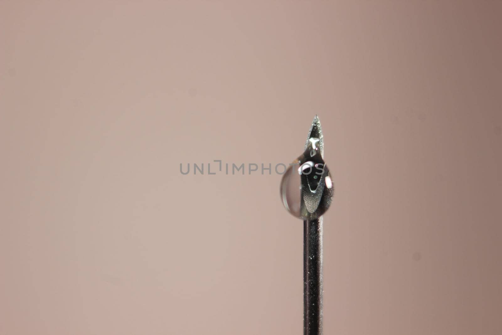 Water drop falling from the syringe needle against grey background by Photochowk