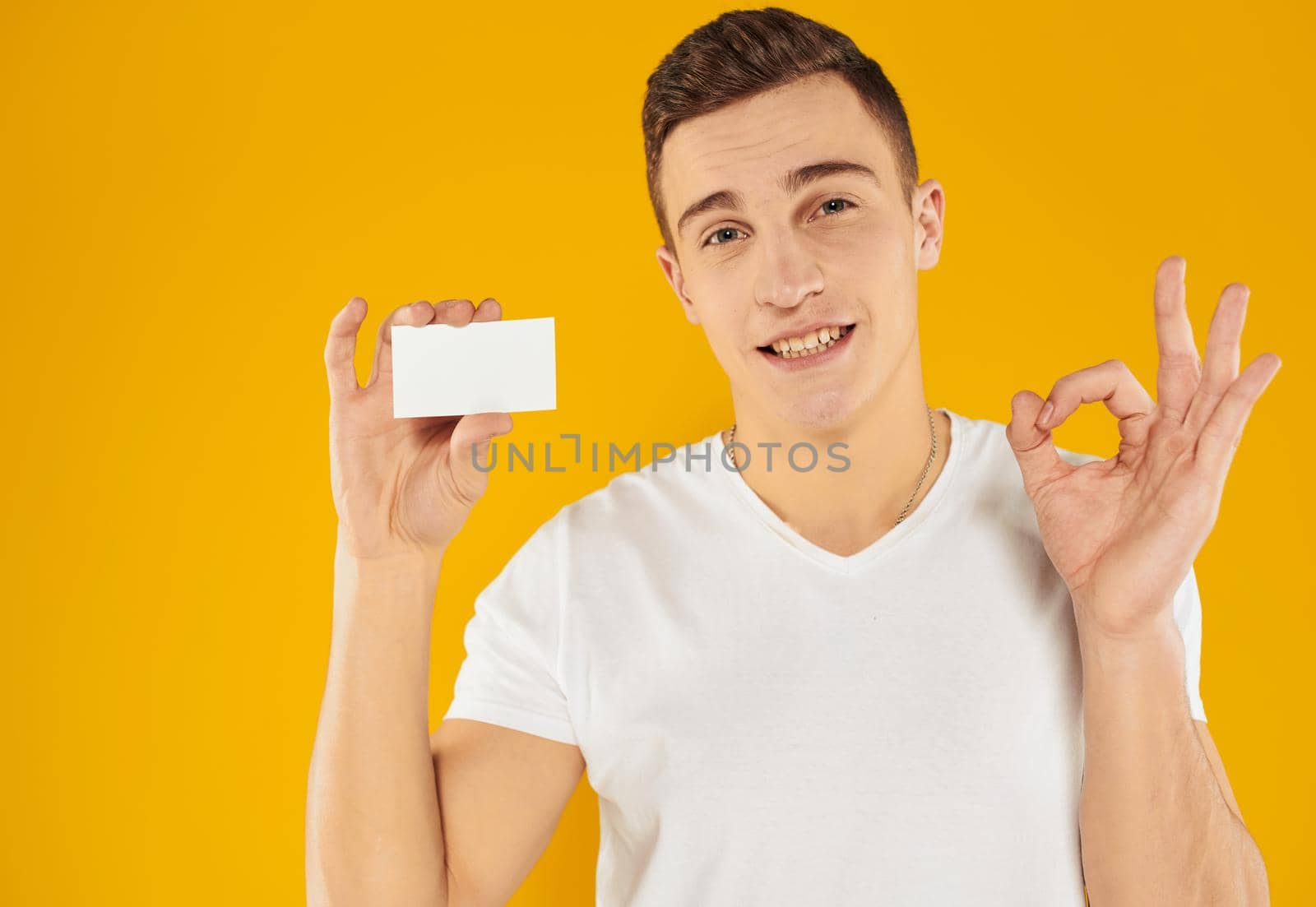 A guy in a white t-shirt shows a credit card on a yellow background cropped view. High quality photo
