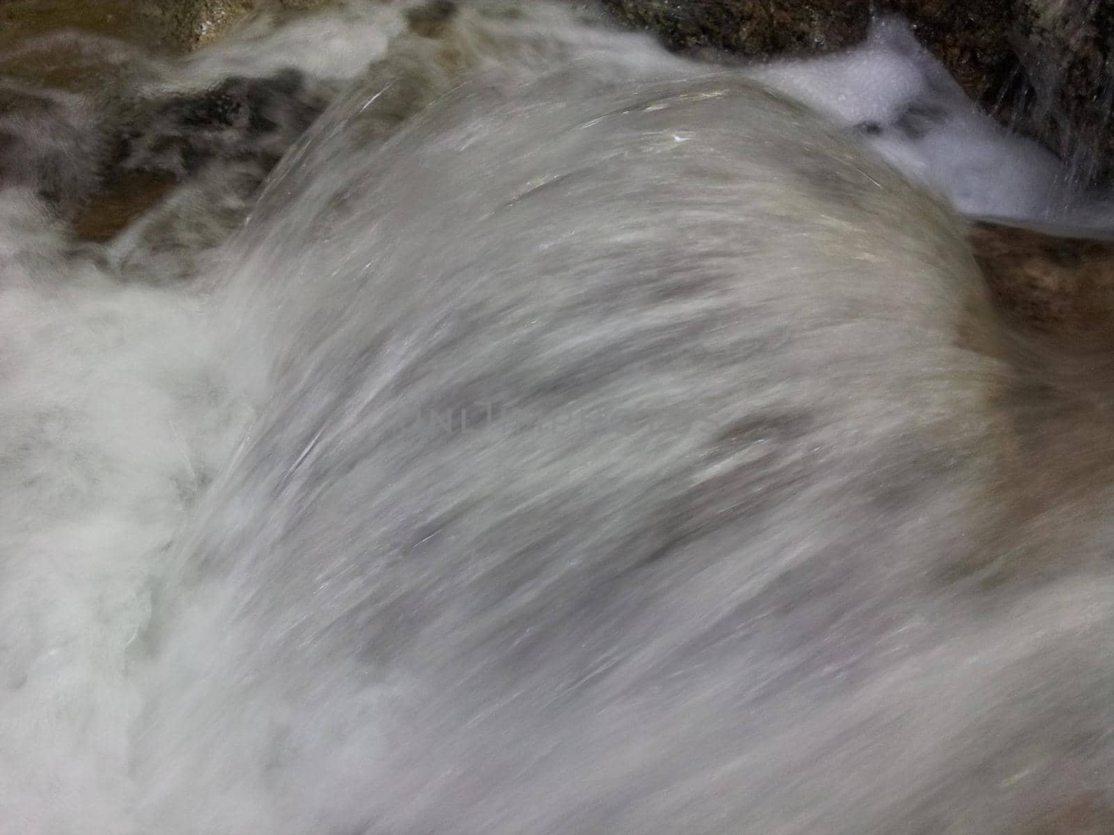 Blurred or unfocused view of flowing water stream in between stones by Photochowk