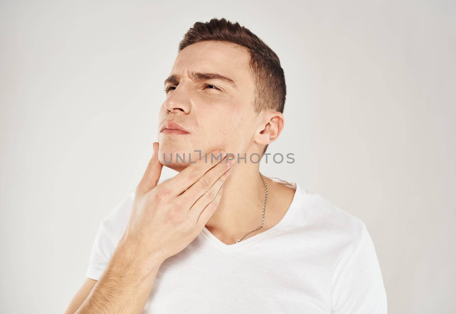 Pensive man in a white T-shirt touches his face with his hand on a light background portrait of a model. High quality photo