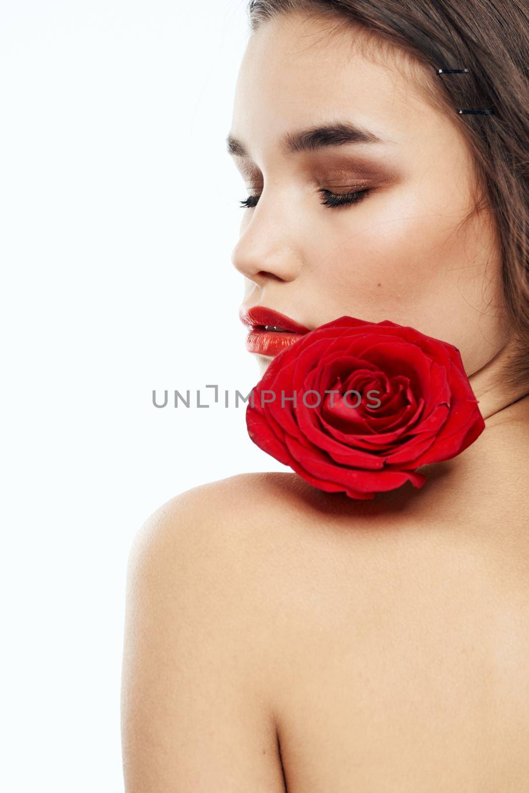 Nude brunette woman with red flower on her shoulder and bright makeup. High quality photo