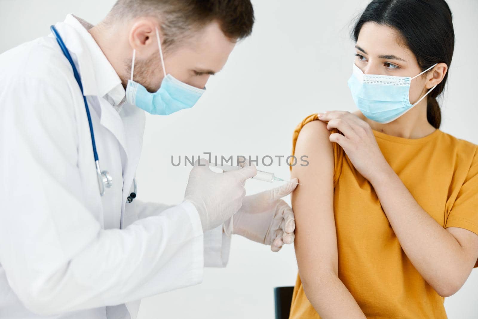 doctor's assistant injections in the shoulder of a woman wearing a medical mask. High quality photo