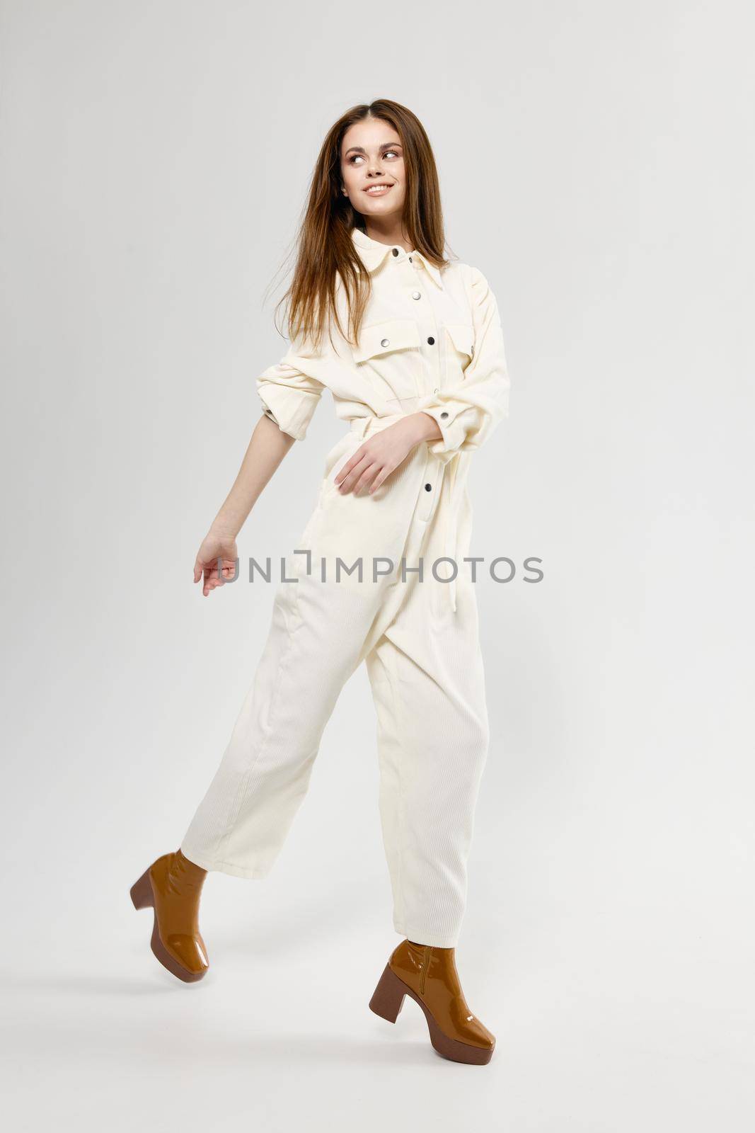 fashionista in overalls and full-length boots on a light background indoors. High quality photo