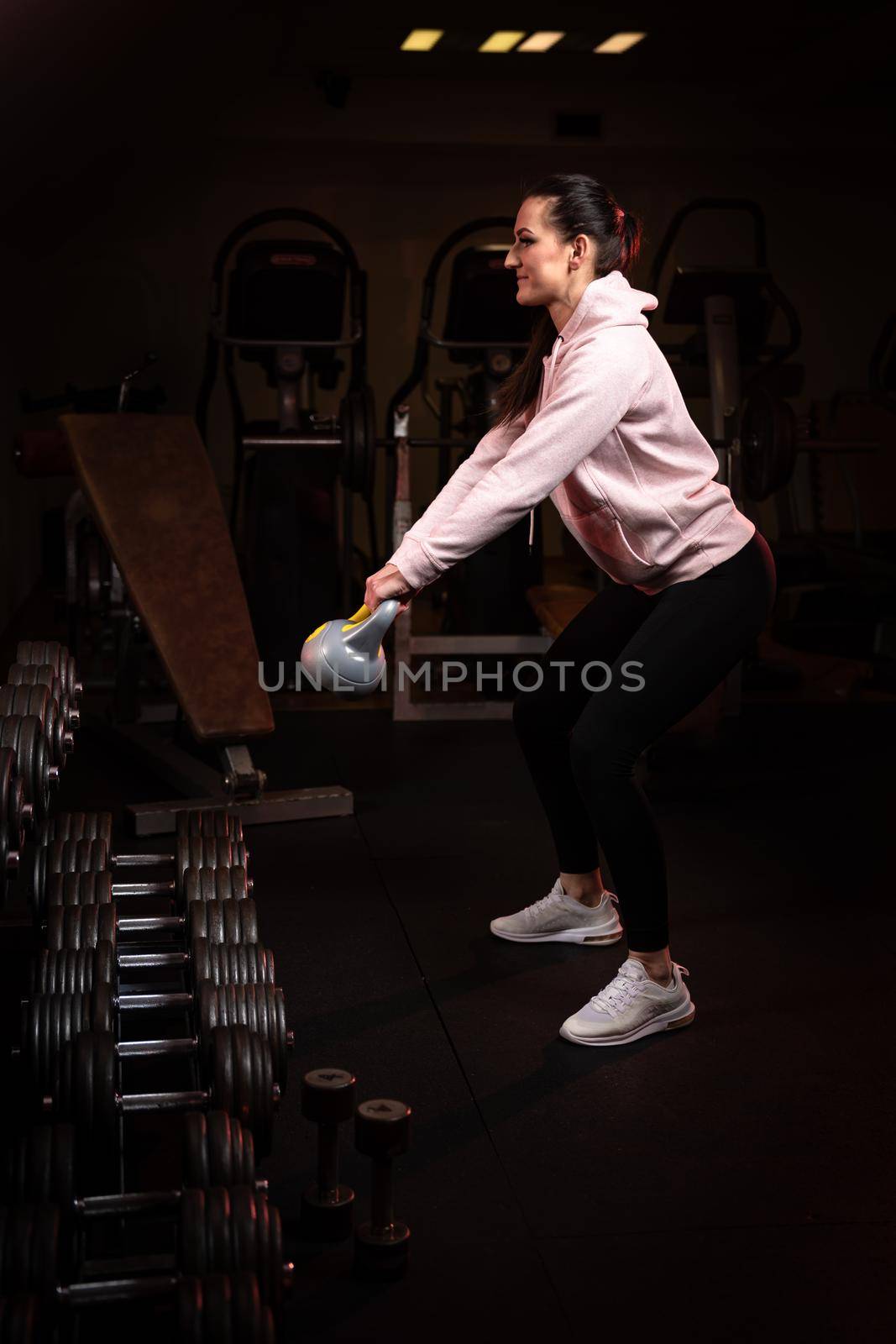 young fitness woman working out with kettlebell in gym by Edophoto