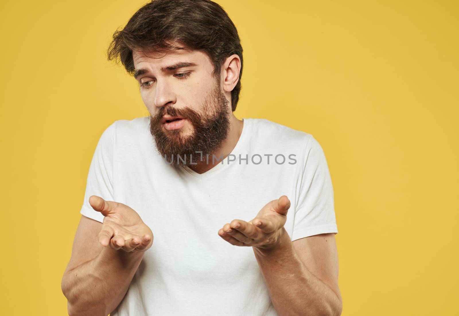 Emotional brunette man gestures with his hands on a yellow background. High quality photo