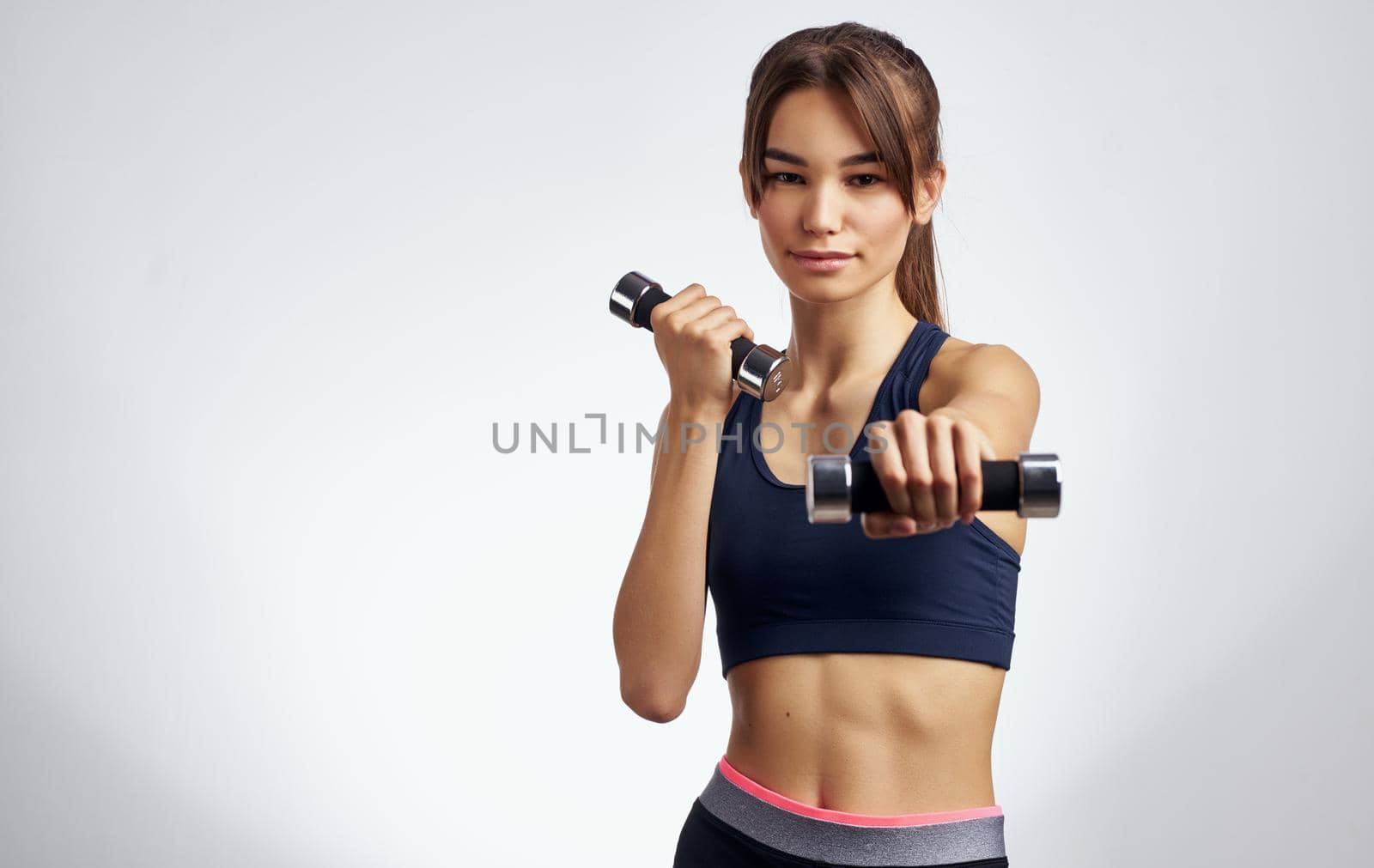 sportswoman with dumbbells on a light background gesturing with her hands fitness model by SHOTPRIME