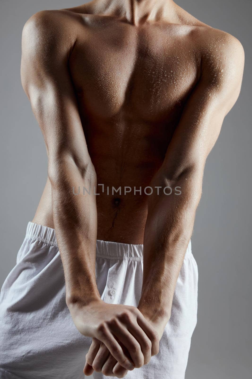 athlete with muscular body in white shorts joined hands on gray background. High quality photo