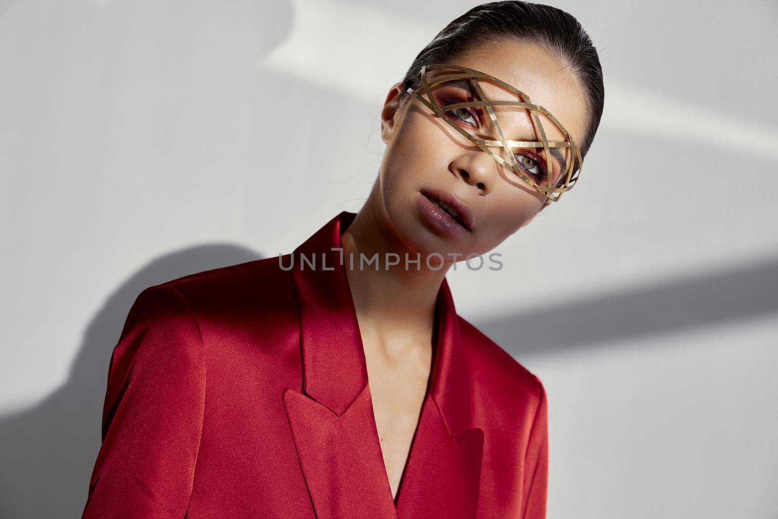 model in a red jacket on a light background looks ahead and jewelry on her face by SHOTPRIME